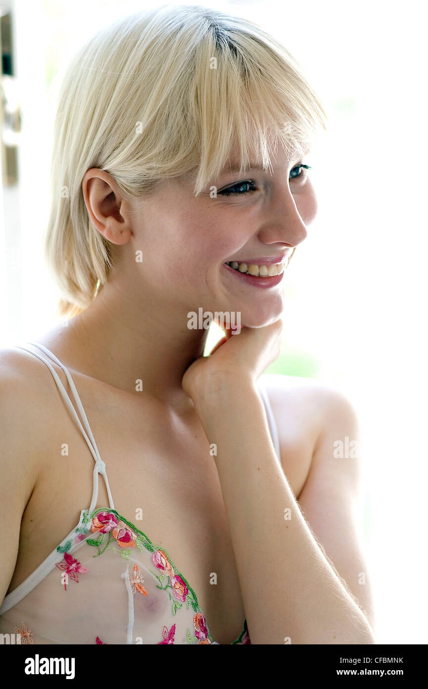 Blonde female fringe wearing a sheer camisole top floral detail, looking to  side hand on neck and smiling teeth showing Stock Photo - Alamy