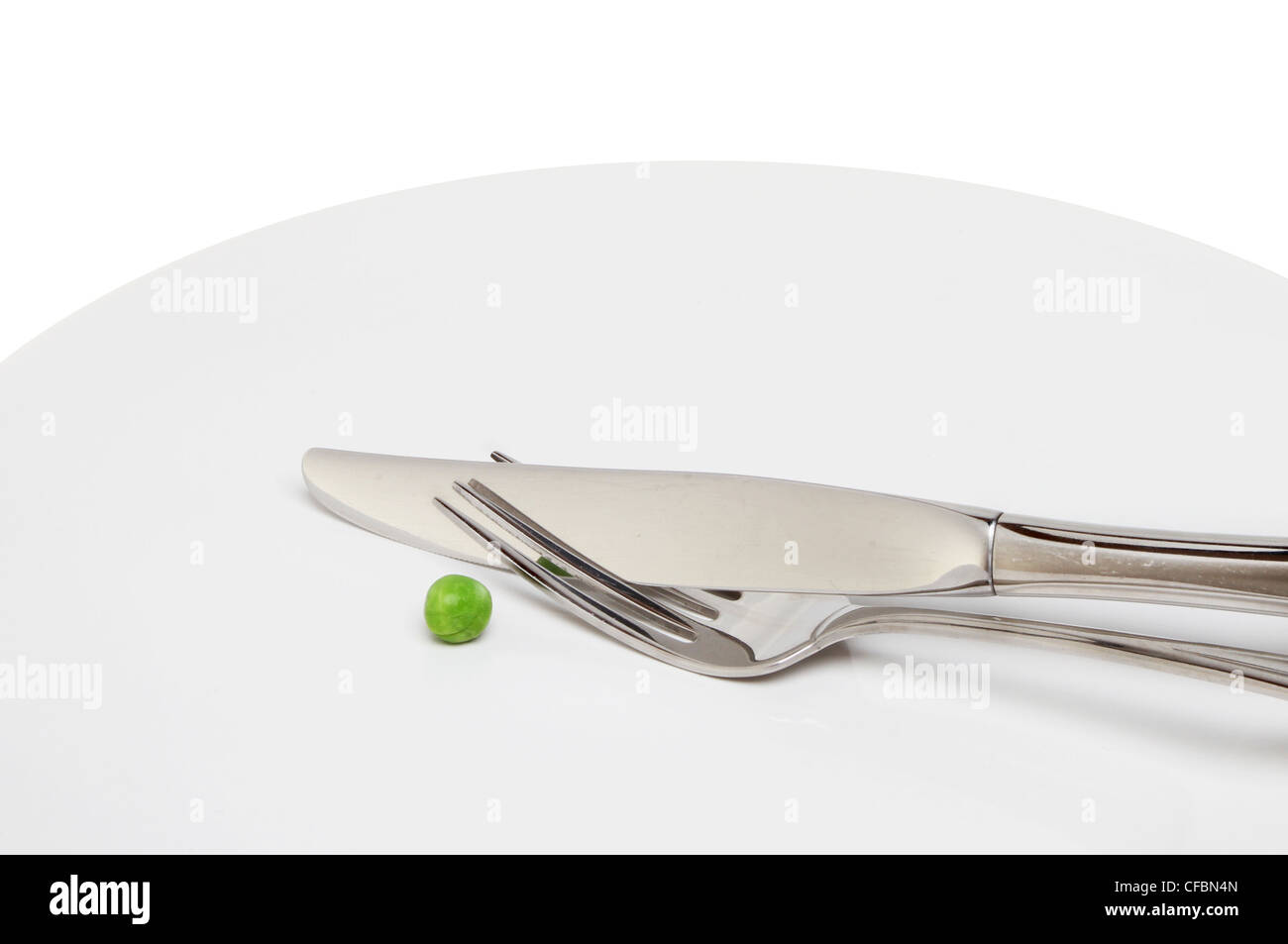 Closeup of a single pea and a knife and fork on a plate Stock Photo