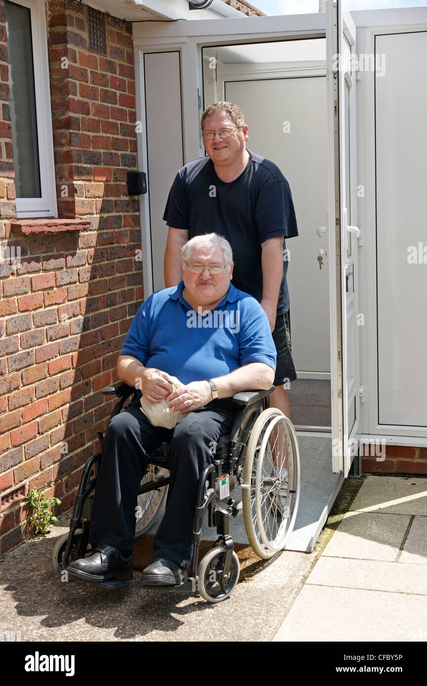 disabled elderly man in wheelchair with his carer son outside their front door Stock Photo