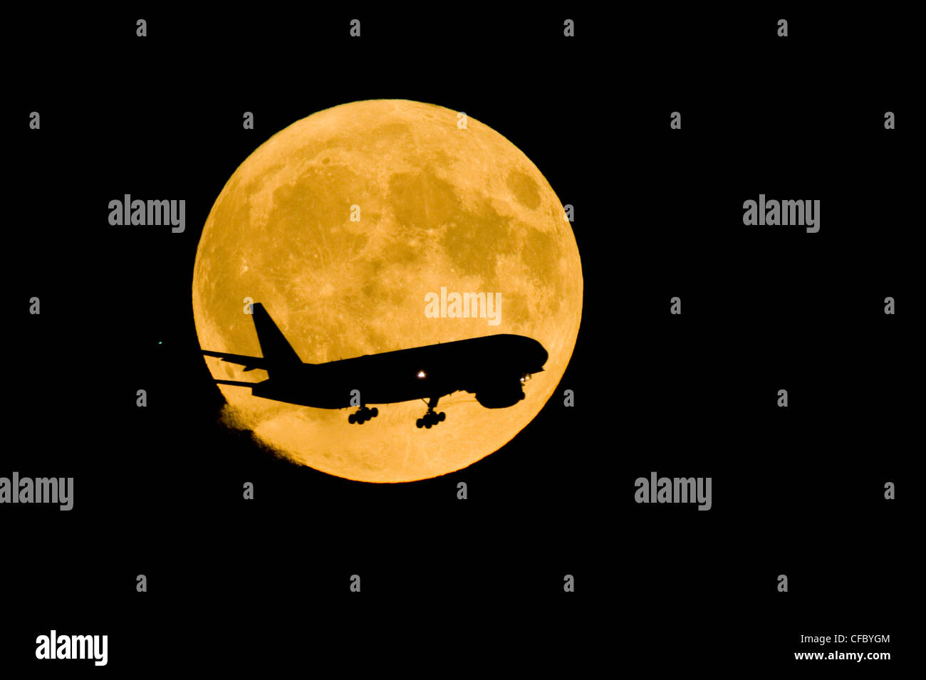 Inbound comercial airliner silhoueted against the full moon. Stock Photo