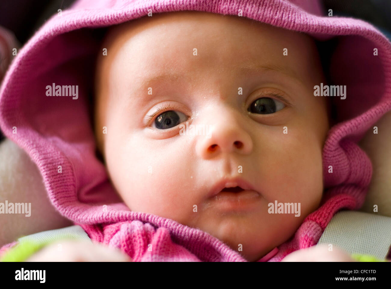 Female two month old baby in a pink hooded jumper with a surprised