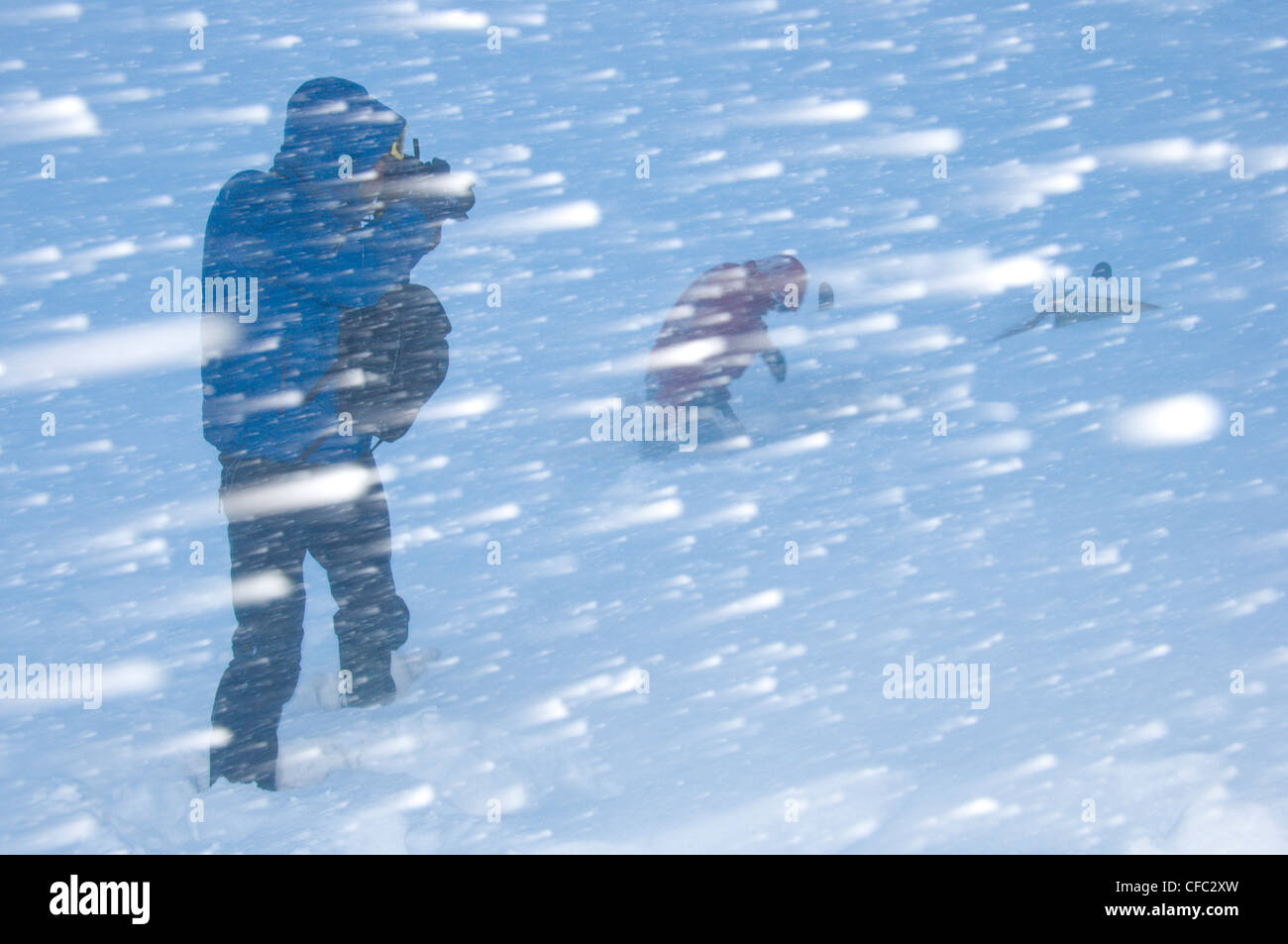 A skier digs out the tent after a six day storm in the Darwin Range, Chile, while a photographer takes a photo in a blizzard Stock Photo