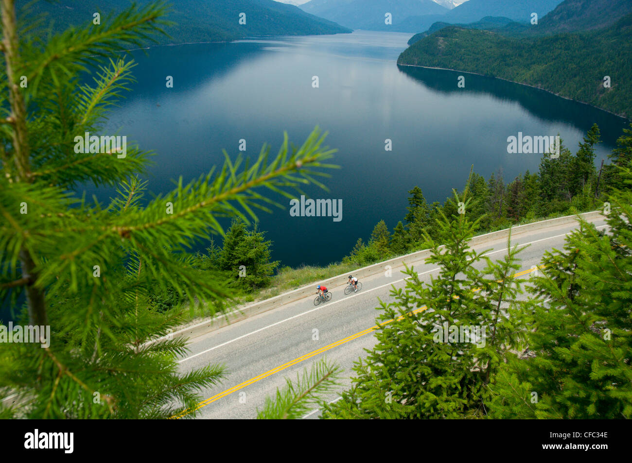 Two women cycling on their road bikes along the cliffy shores of Slocan Lake, British Columbia, Canada Stock Photo
