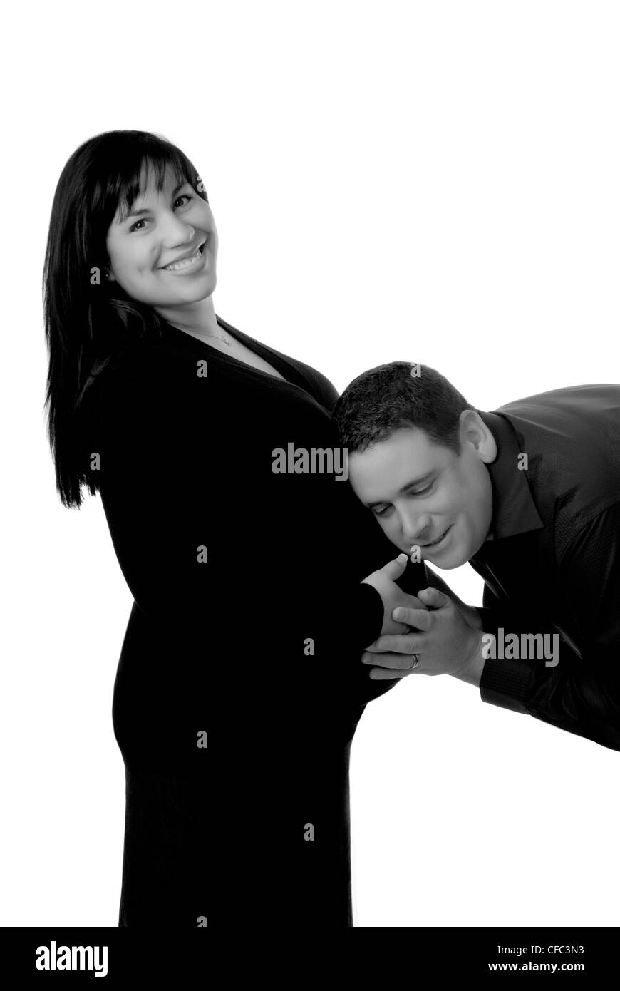 A fun maternity black and white image of father with ear to wife's pregnant belly. Stock Photo