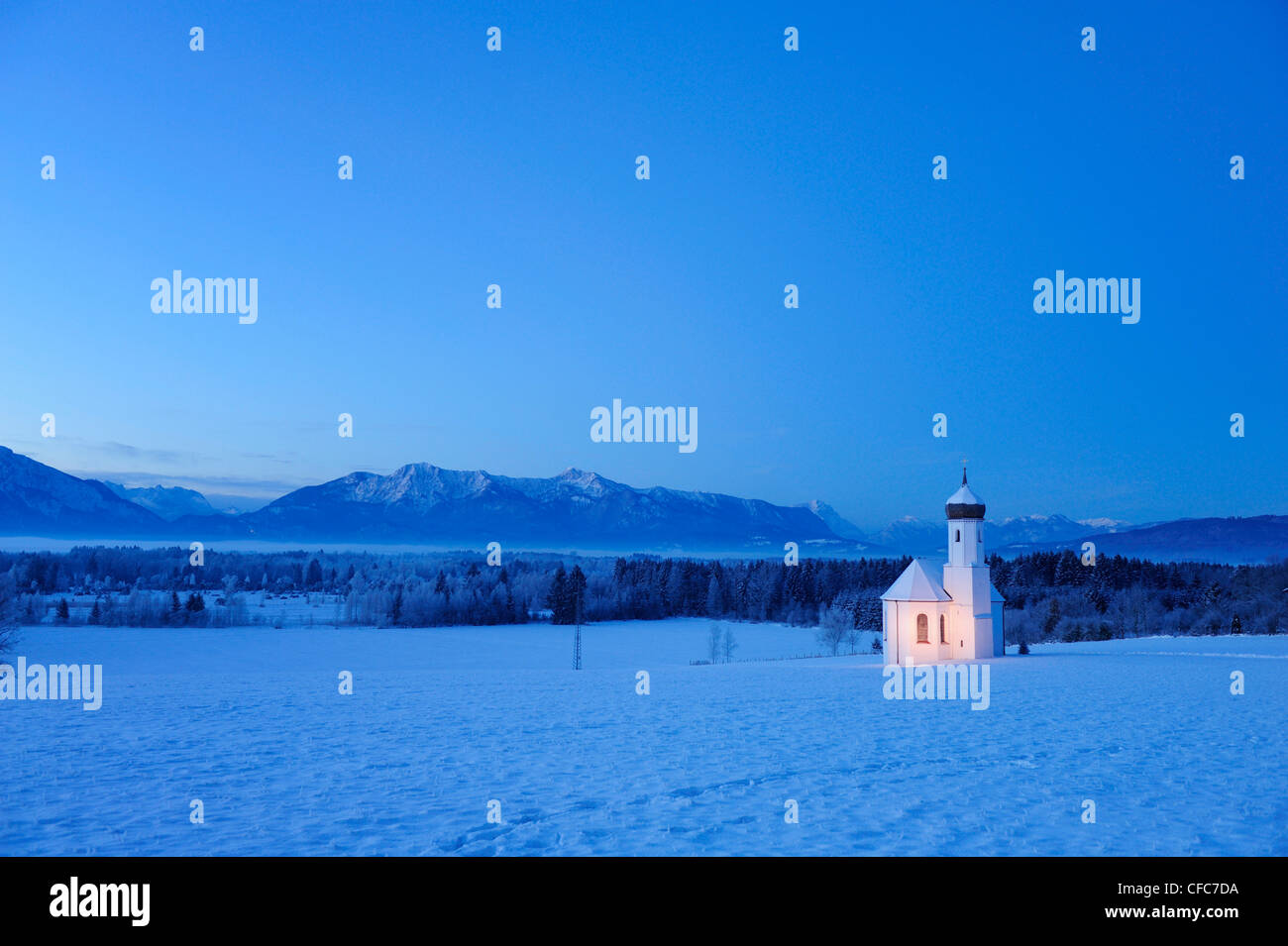Snow covered church in front of range of Alps in the evening, Penzberg, Werdenfelser Land, Upper Bavaria, Bavaria, Germany, Euro Stock Photo