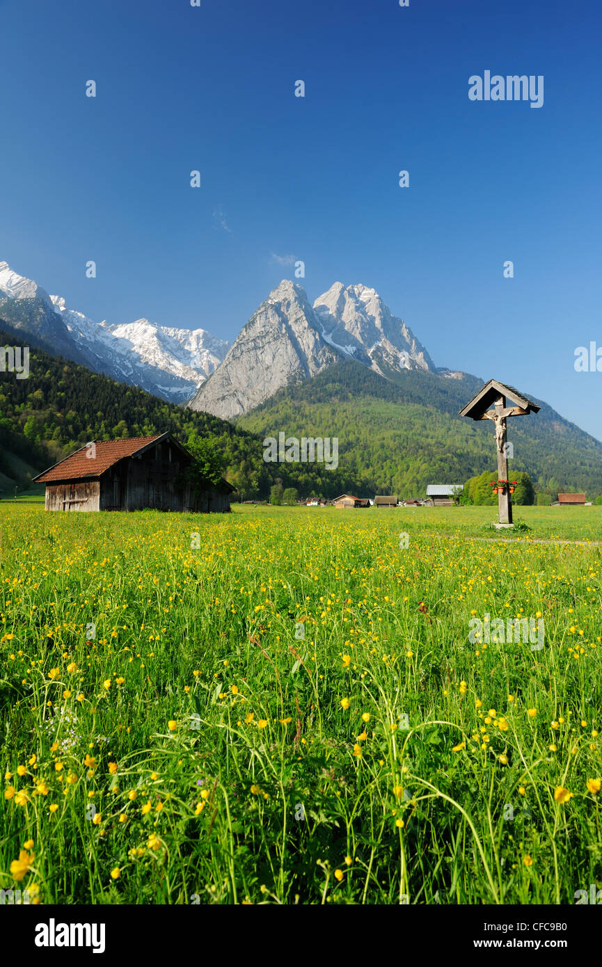 Meadow with flowers, hay sheds and wayside cross in front of Zugspitze range with Waxenstein, Garmisch-Partenkirchen, Wetterstei Stock Photo