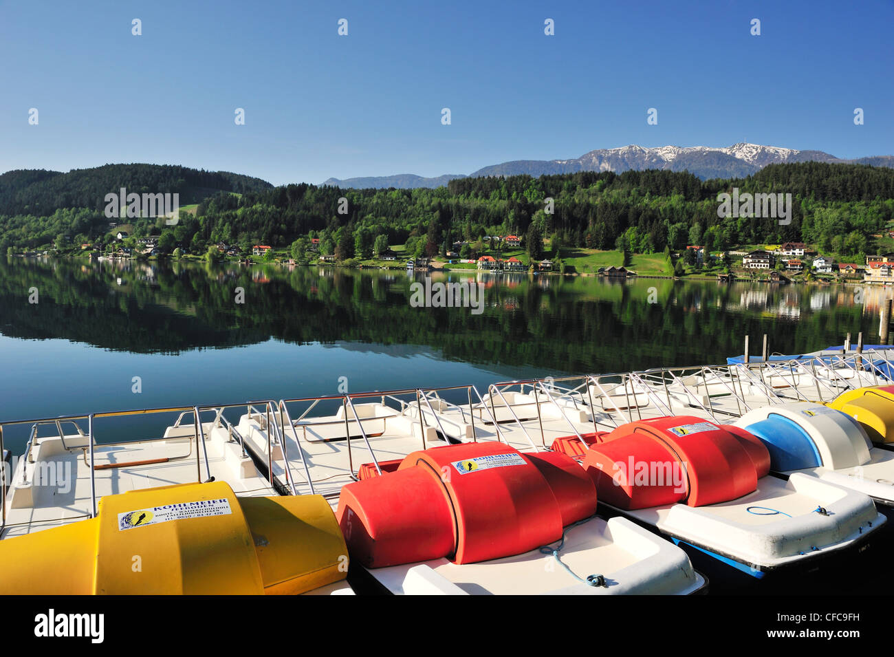 Multicolored pedal boats at lake Millstaetter See with snow covered mountains in the background, Seeboden, lake Millstaetter See Stock Photo