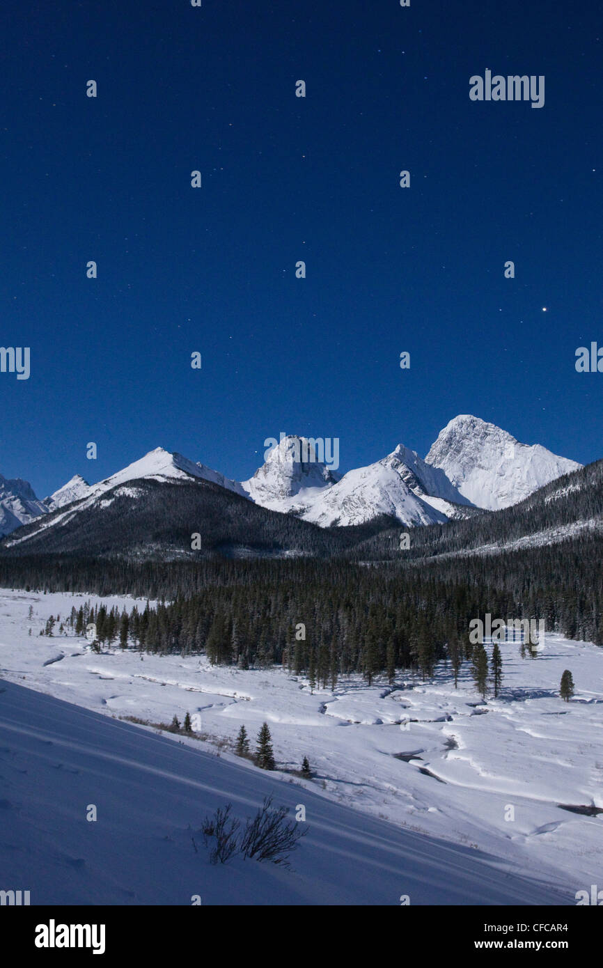 The Rocky Mountains illuminated by a full moon on a winter night in Spray Valley Provincial Park in Kananaskis Country, Alberta. Stock Photo