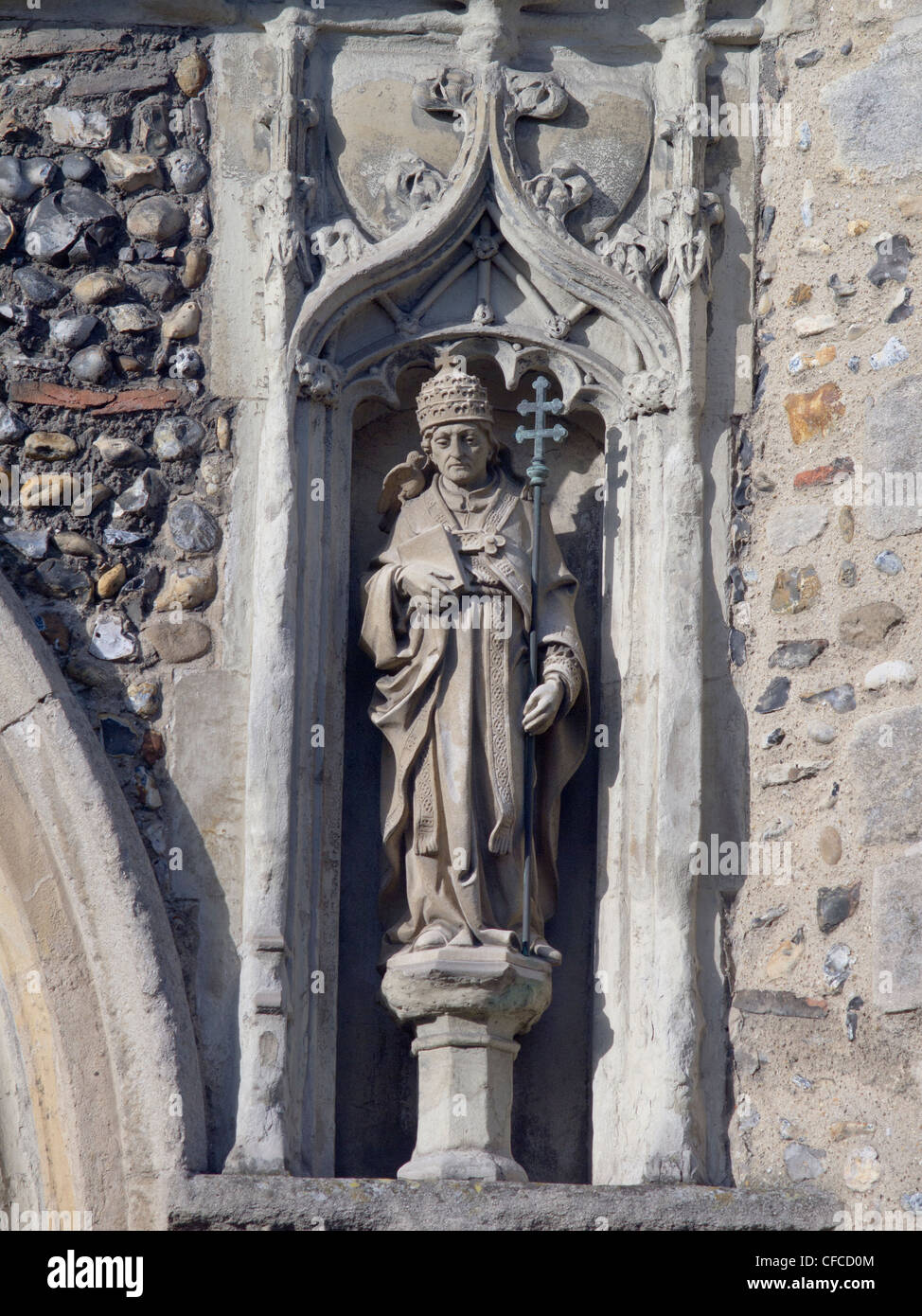 A stone statue of a Christian saint, wearing robes and holding a staff, set into the wall of a church. Stock Photo
