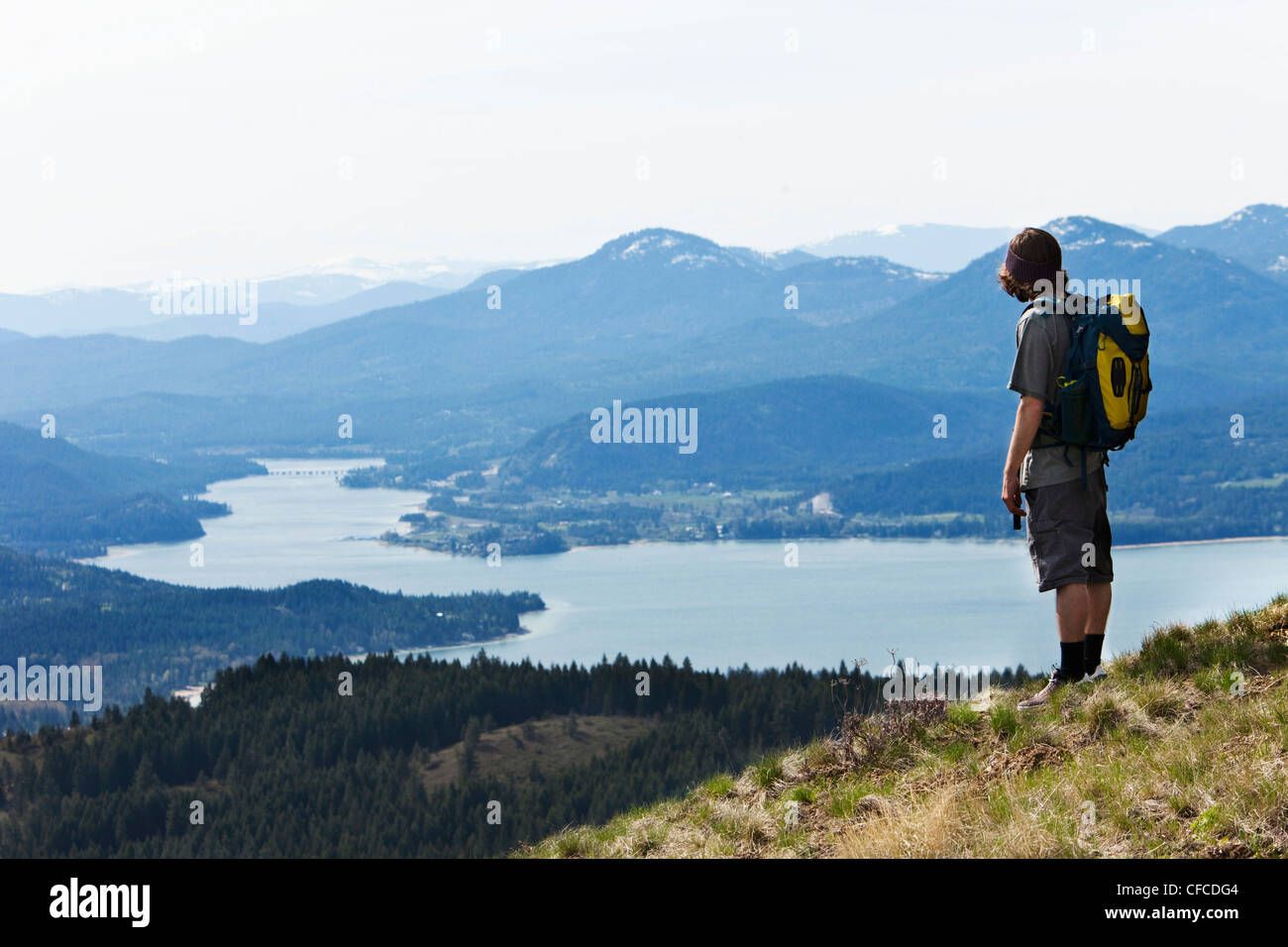 A young man backpacking looks out over a large river and Sandpoint, Idaho. Stock Photo
