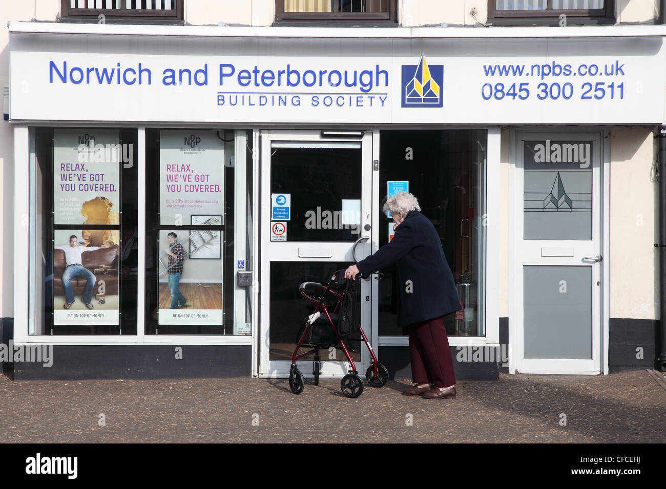 Senior woman with walking frame about to enter Norwich and Peterborough Building Society Watton Norfolk England Stock Photo