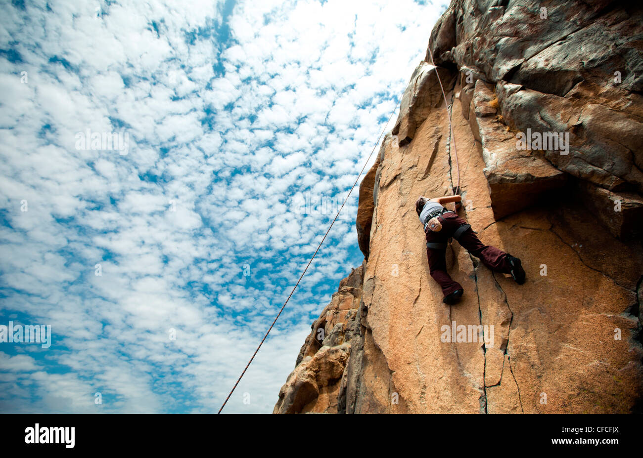 Looking up at a woman climber a crack seam in a granite cliff face. Stock Photo