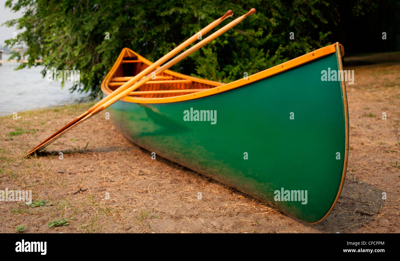 A portaged, green cedar canvas canoe and paddles. Stock Photo