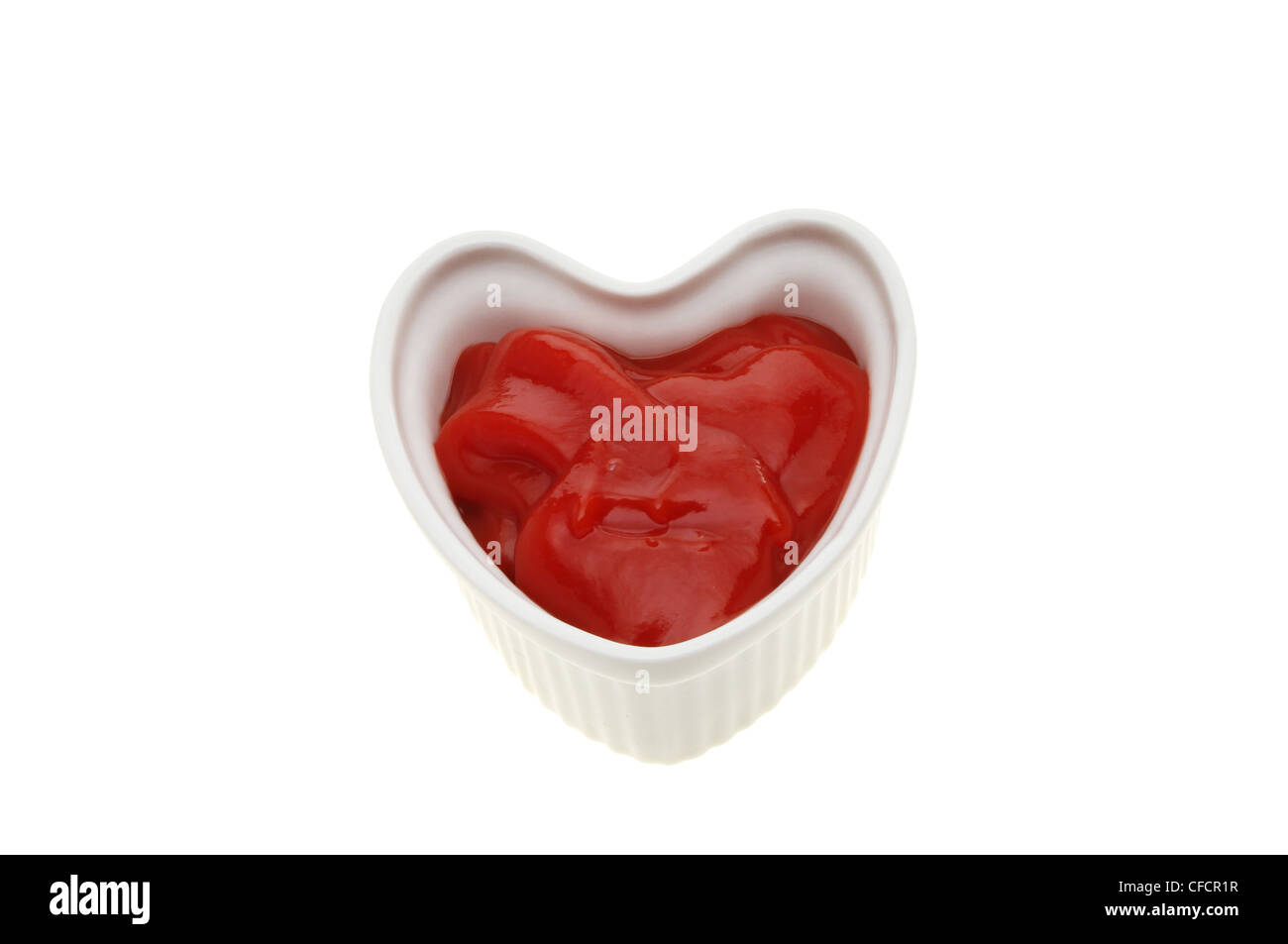 Tomato ketchup in a heart shaped ramekin isolated against white Stock