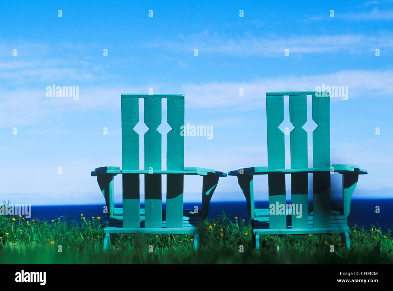 Green wooden lawn chairs sit on lawn by oceanside vista, British