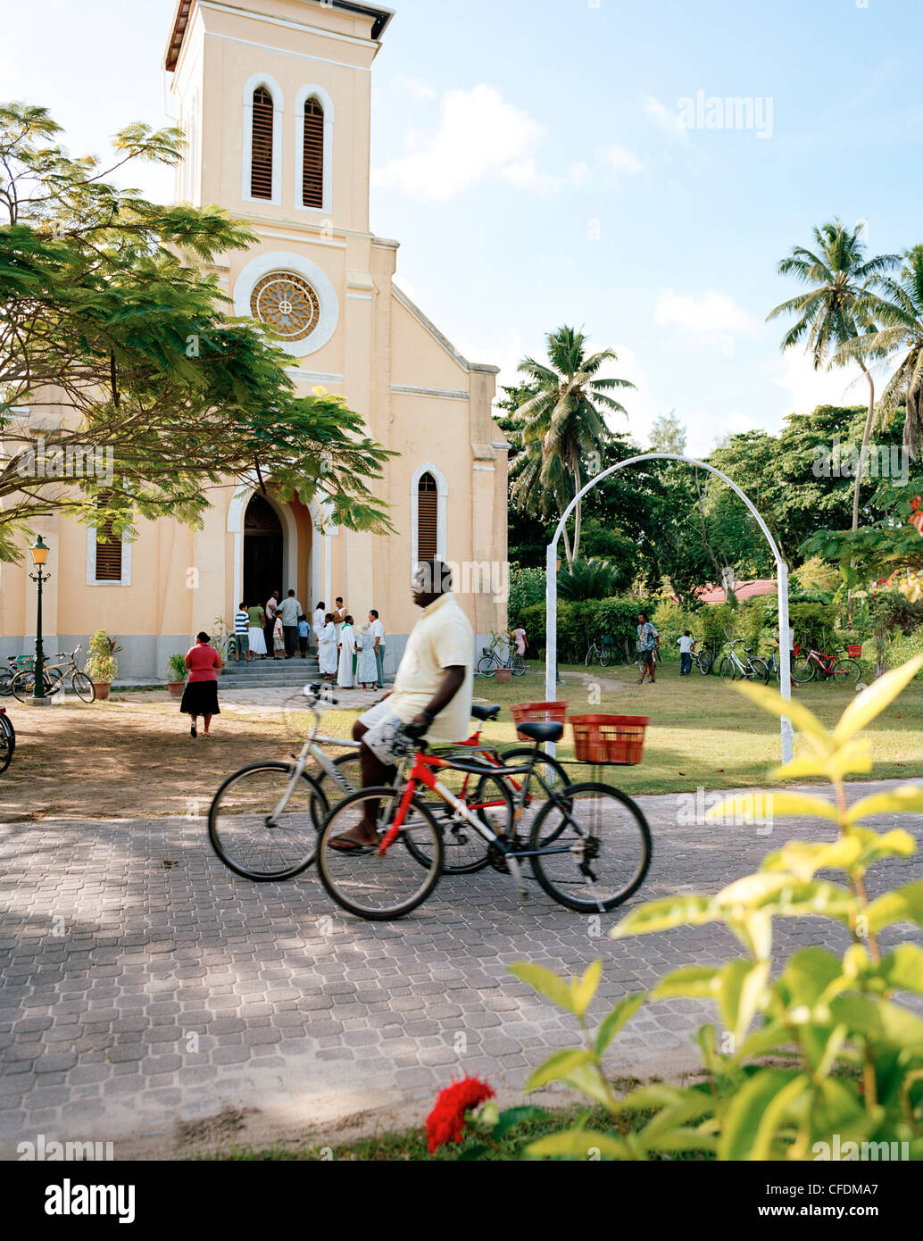 Man with rental bikes passing in front of the church at La Passe, La Digue, La Digue and Inner Islands, Republic of Seychelles, Stock Photo