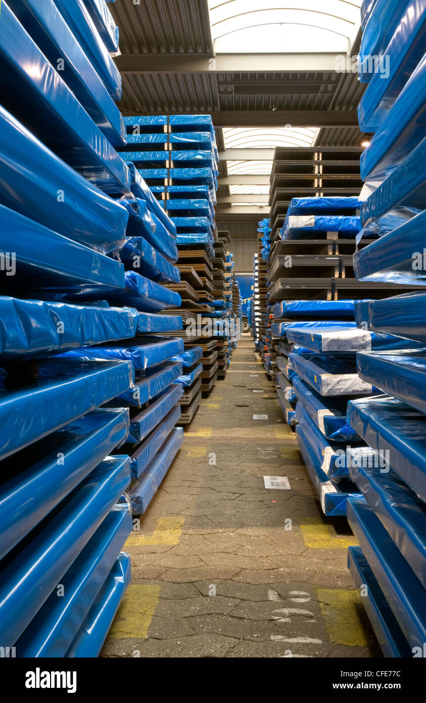 Large warehouse interior with packaged steel sheet on pallets, looking through an aisle. Stock Photo