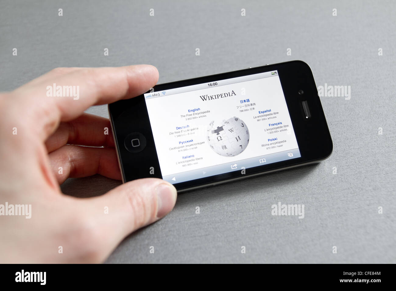 Man hand holding Apple iPhone with Wikipedia start page on a screen. Stock Photo