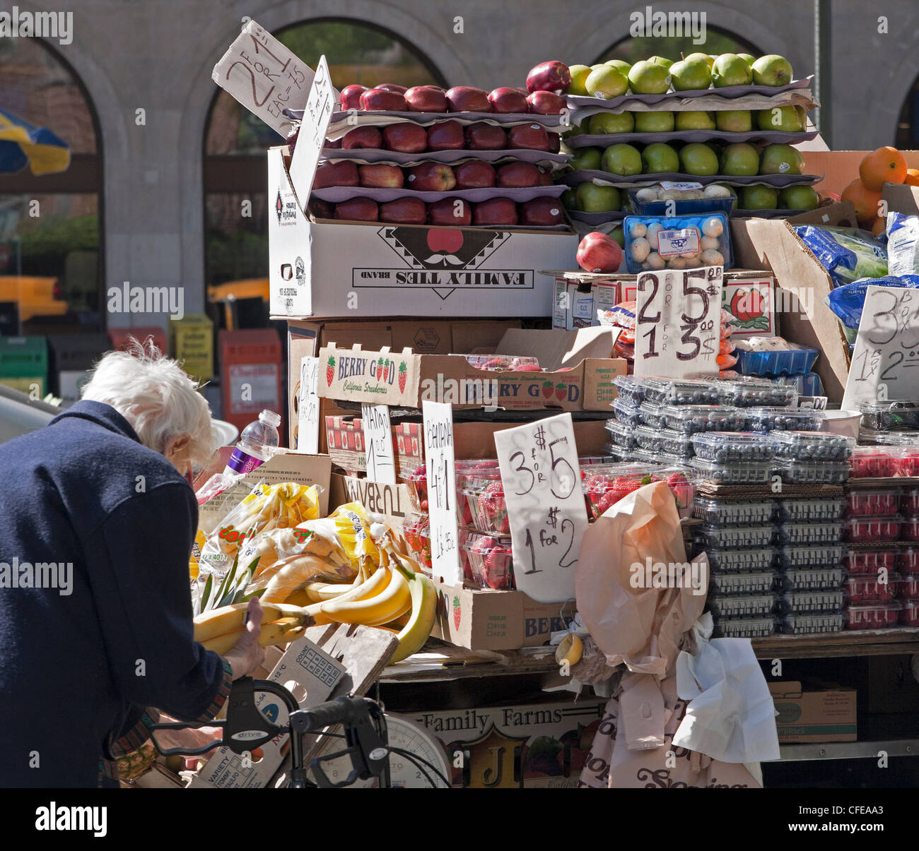 A woman inspects bananas at a fruit stand in an urban market. Stock Photo