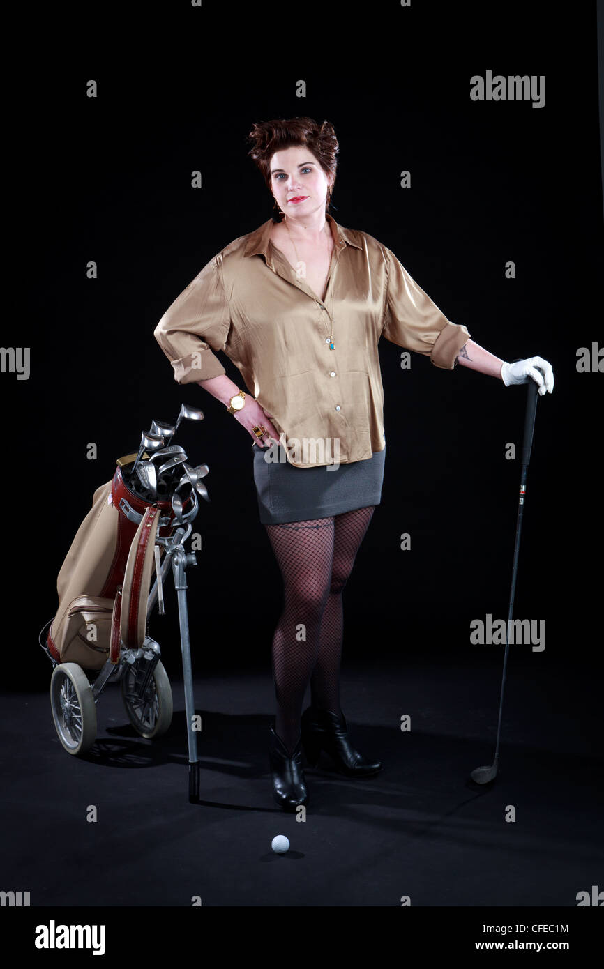 Elegantly dressed woman poses with golf clubs in front of black backdrop Stock Photo