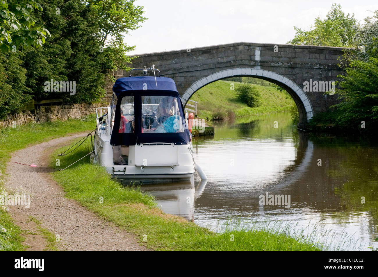 Pleasure cruiser (boat) moored in scenic rural area by small stone bridge on banks of Leeds Liverpool Canal - Gargrave, North Yorkshire, England, UK. Stock Photo