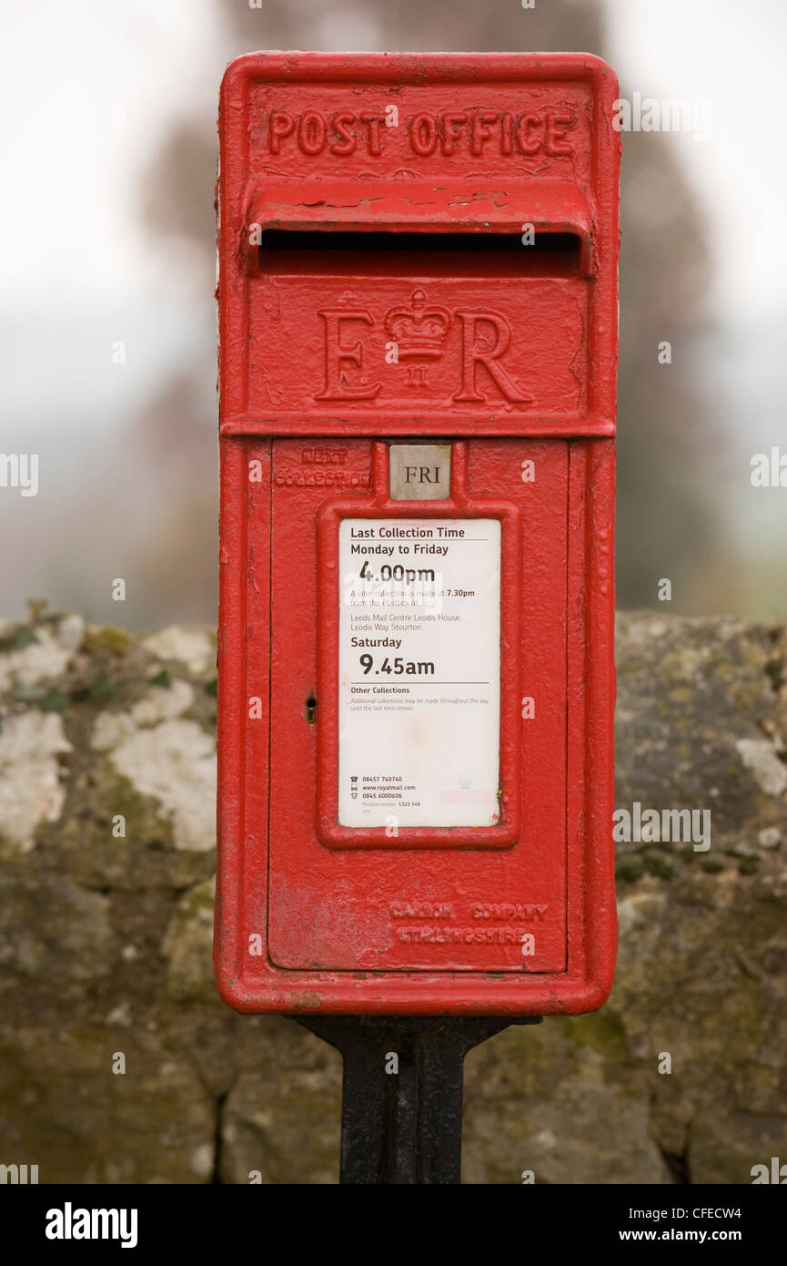 Close-up front view of bright red post box (lamp box style, marked ER) standing in front of drystone wall - Leathley, North Yorkshire, England, UK. Stock Photo