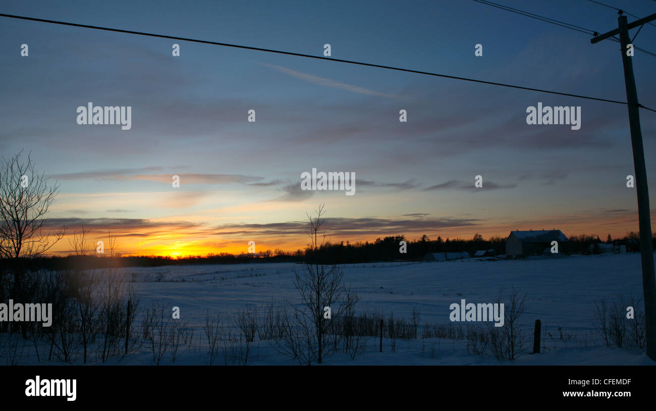 Sunset horizontal silhouette image of snow covered fields with a farm in the distance. Stock Photo