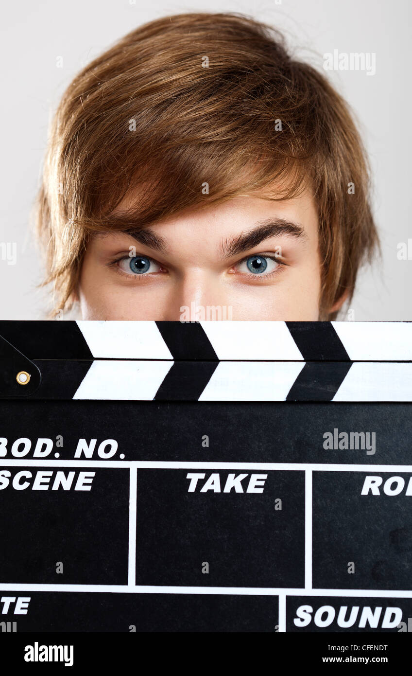 Portrait of a young man peeking behind a clapboard, over a gray background Stock Photo