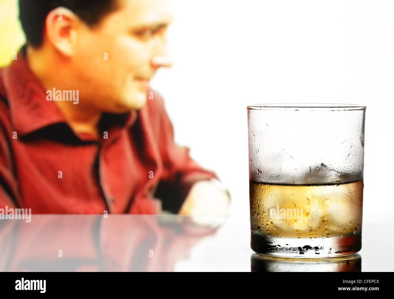 Glass of whiskey with ice and defocused male in the background Stock Photo