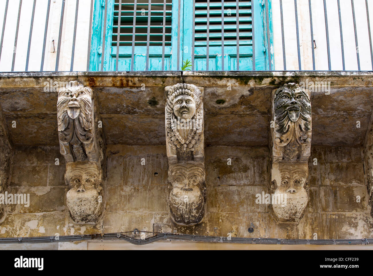 Balcony in the typical Silician Baroque style supported by grotesque masks and putti, and with a wrought iron balustrade. Stock Photo