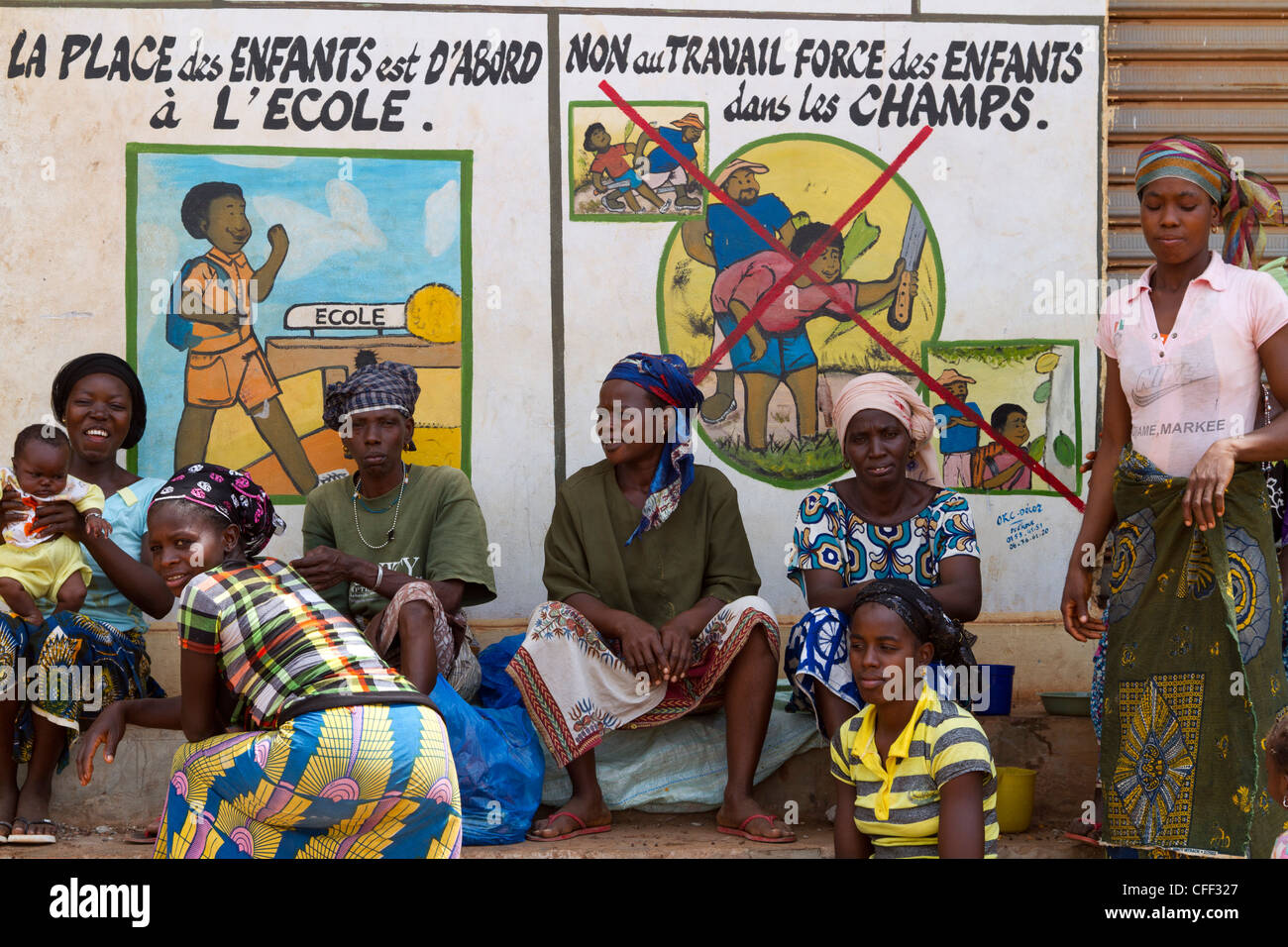 Women waiting to sort beans of cacao in front of a public notice again the child labor ,Duekoue, Ivory Coast ,West Africa Stock Photo