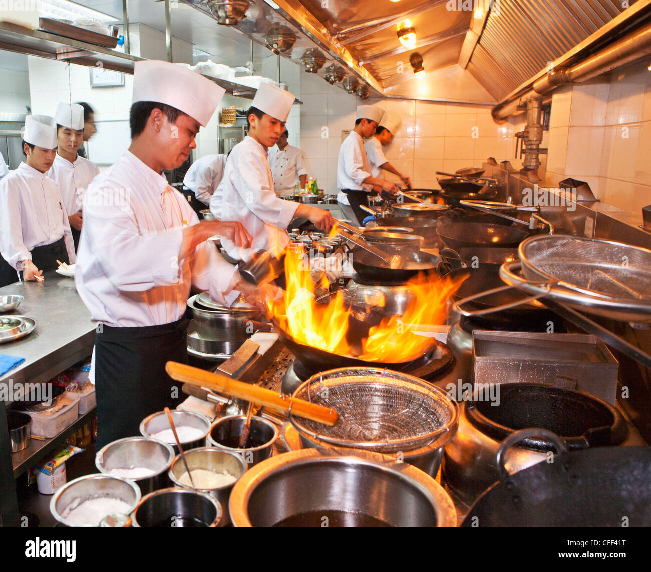 Chefs preparing Chinese cuisine in woks in the modern kitchen of a