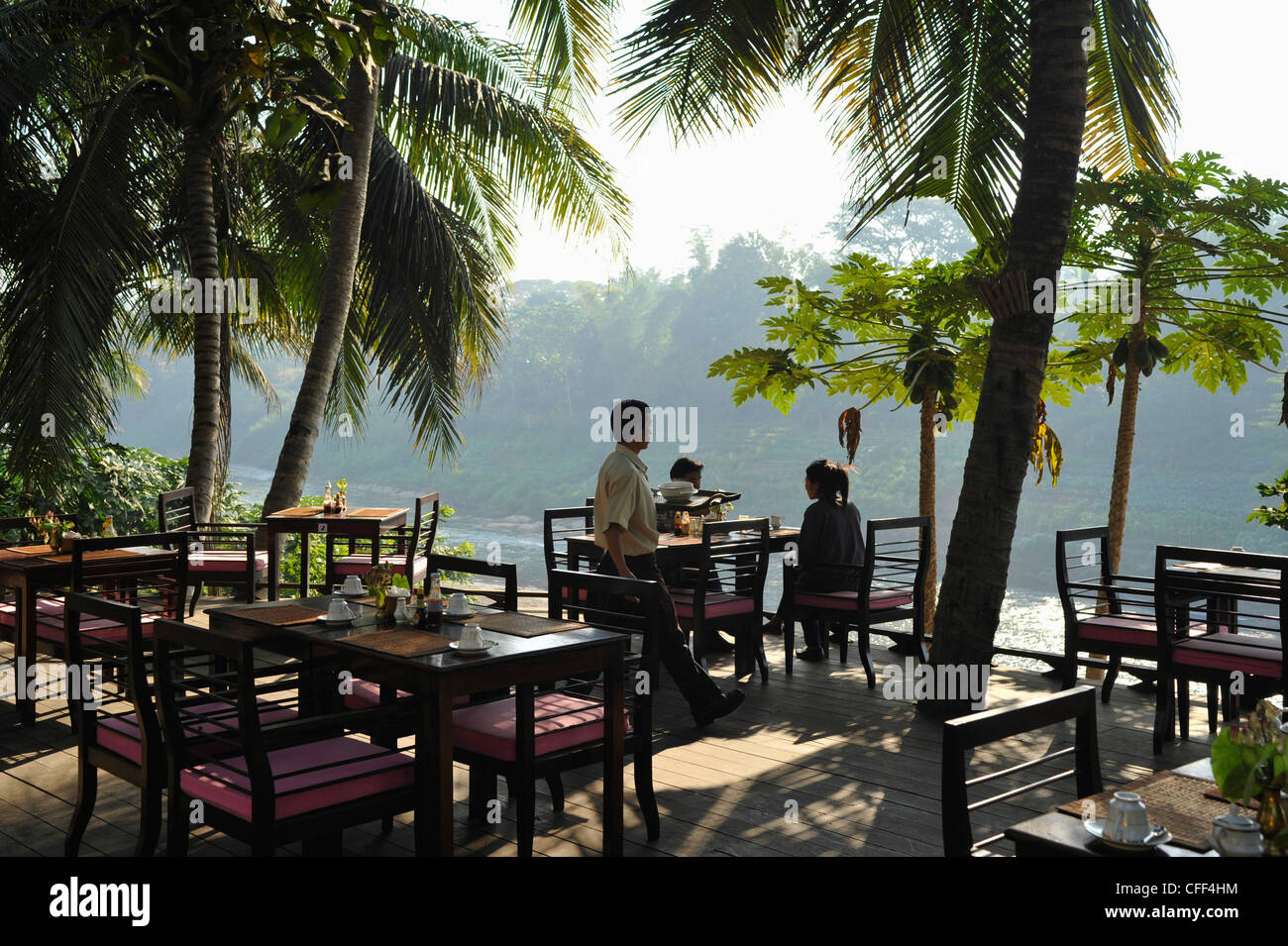 Restaurant terrace under palm trees at Nam Khan river, tributary to Mekong river, Luang Prabang, Laos, Lao Peoples Democratic Re Stock Photo