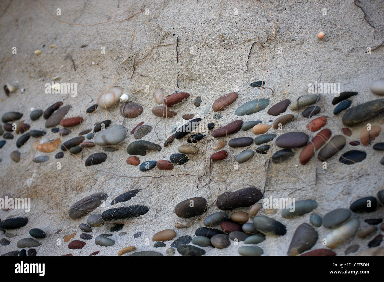A vertical sand bank at the beach with bands of pebbles being exposed Stock Photo
