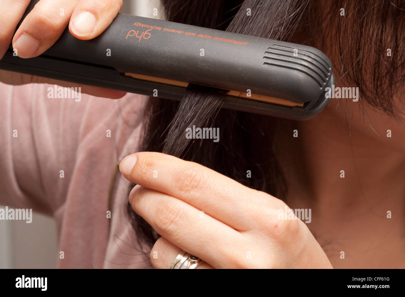 Woman using hair straighteners to style her hair. Stock Photo