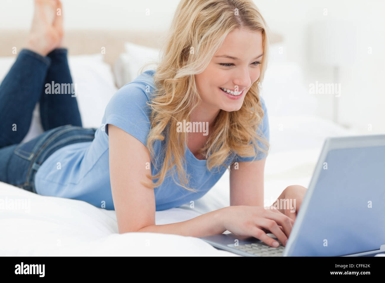 Woman lying on the bed with her laptop smiling Stock Photo - Alamy