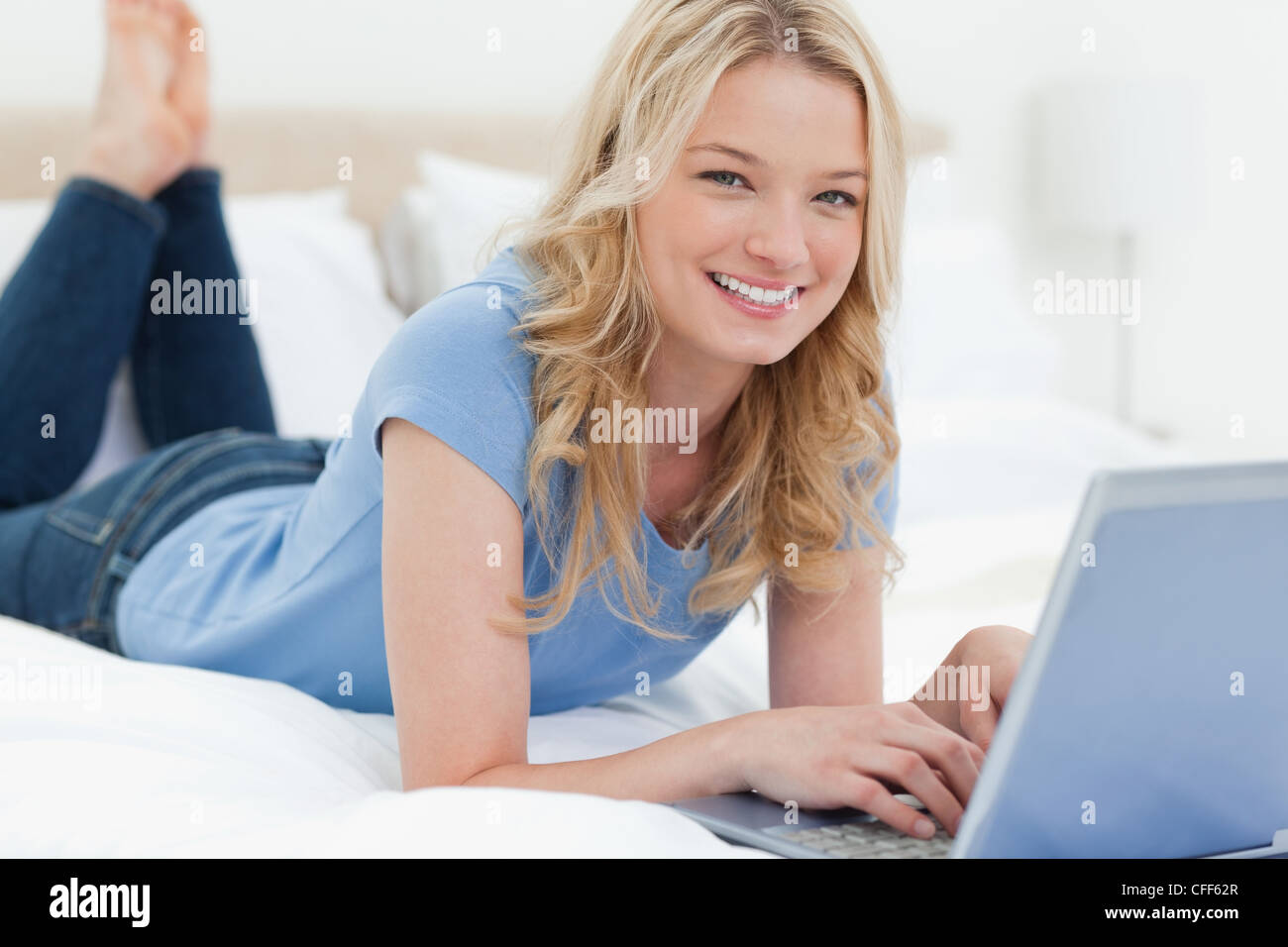 Woman lying on a bed smiling as she uses her laptop Stock Photo - Alamy