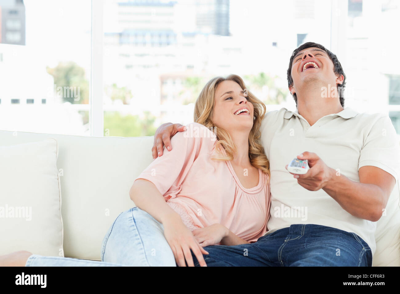 Man and woman on the couch laughing at the tv programme Stock Photo