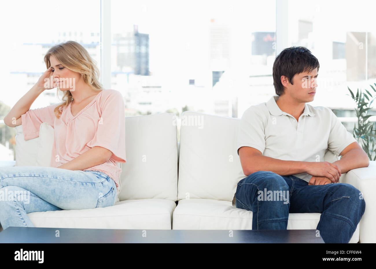 Man and woman sitting at opposite ends of then couch, both looking