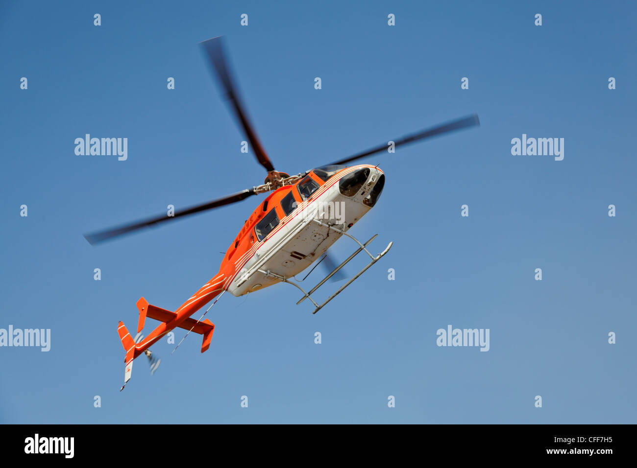 hovering orange and white helicopter in clear blue sky over Katra Heliport in Northern Indian Himalayas, photograph rendition Stock Photo