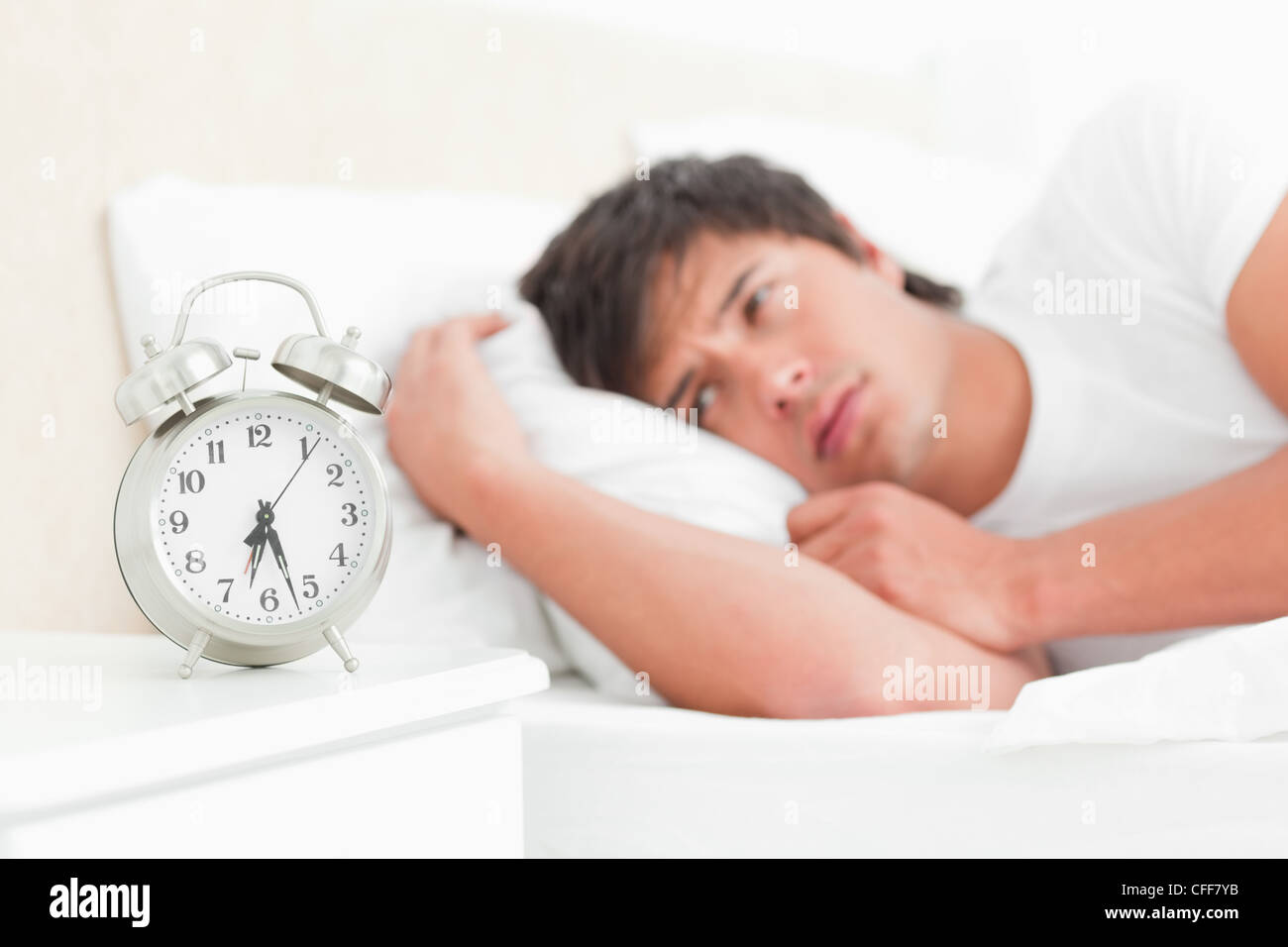 Man in bed waking up not looking happy with his ringing alarm clock Stock Photo Alamy