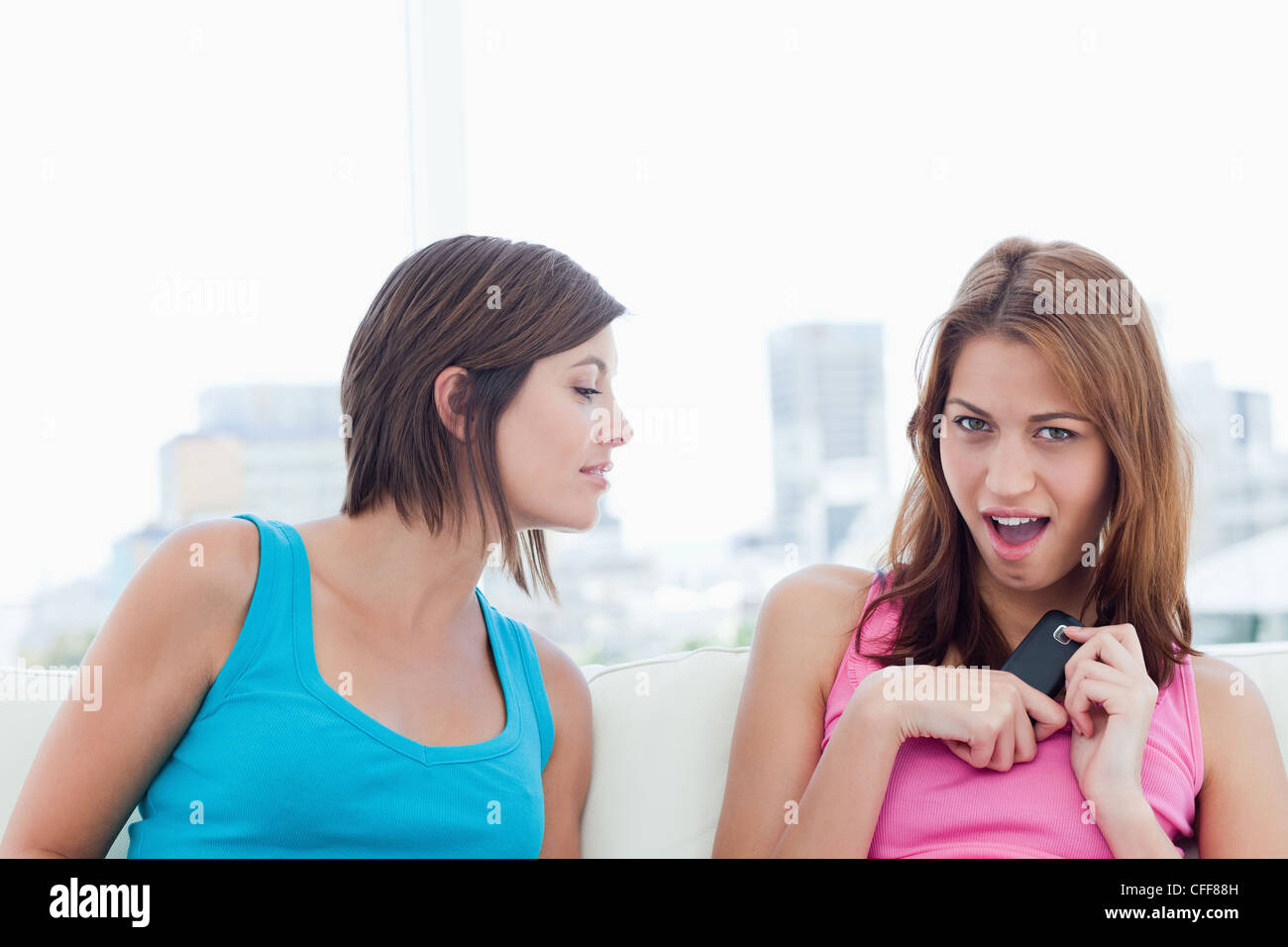 Woman trying to look at a mobile phone hidden by her friend Stock Photo