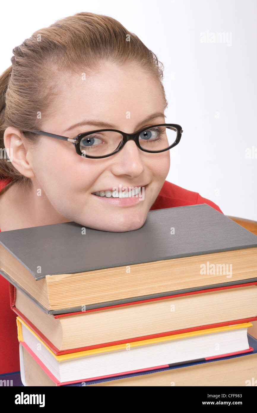 Young high school schoolgirl in spectacles sitting in library with and resting her chin on big pile of textbook Stock Photo
