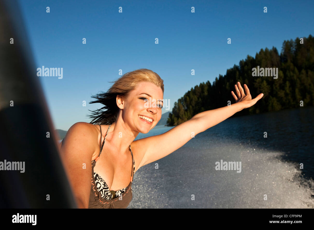 A beautiful young women smiling and holding her hand out at sunset on a wakeboarding boat in Idaho. Stock Photo