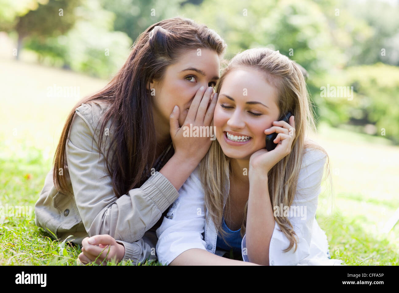 Young woman talking on the phone while being told a secret Stock Photo