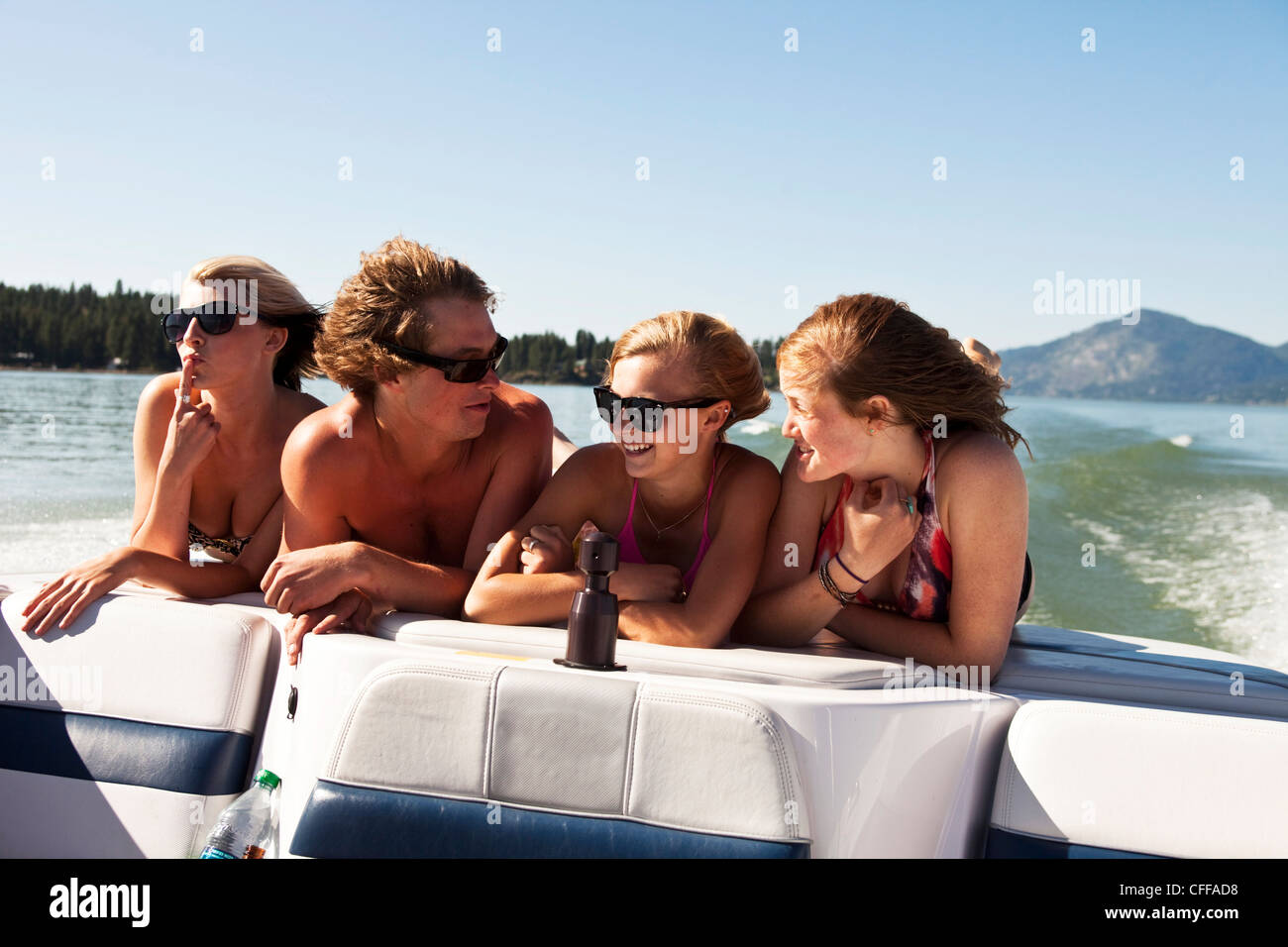 Four young adults laughing and smiling on the back of a wakeboard boat on a lake in Idaho. Stock Photo
