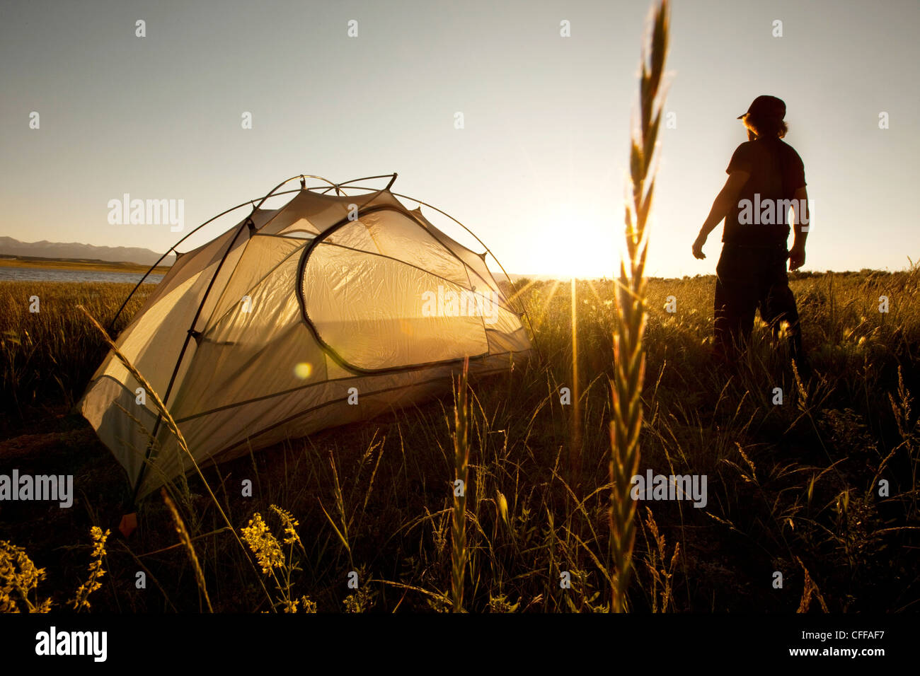 A man standing next to his tent at sunset on a backpacking trip in the mountains of Montana. Stock Photo