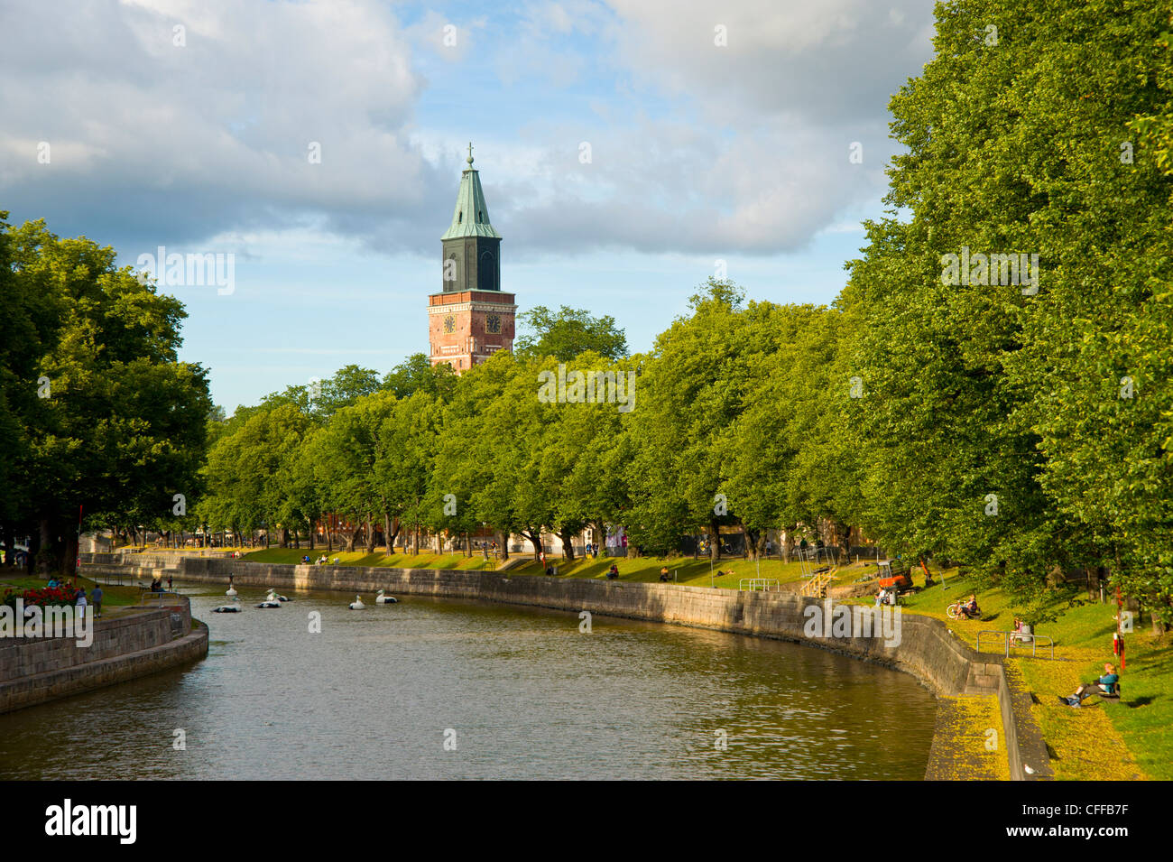 People relax on the banks of river Aura (Aurajoki), Turku Finland with the Cathedral spire on the skyline Stock Photo