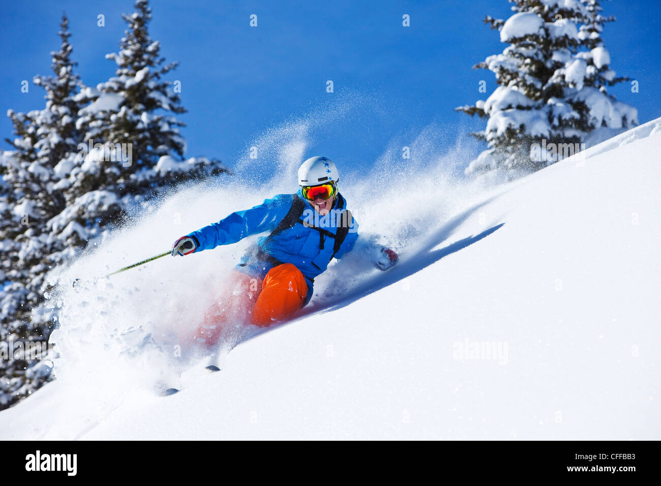 A athletic skier smiling rips fresh powder turns in the backcountry on a sunny day in Colorado. Stock Photo