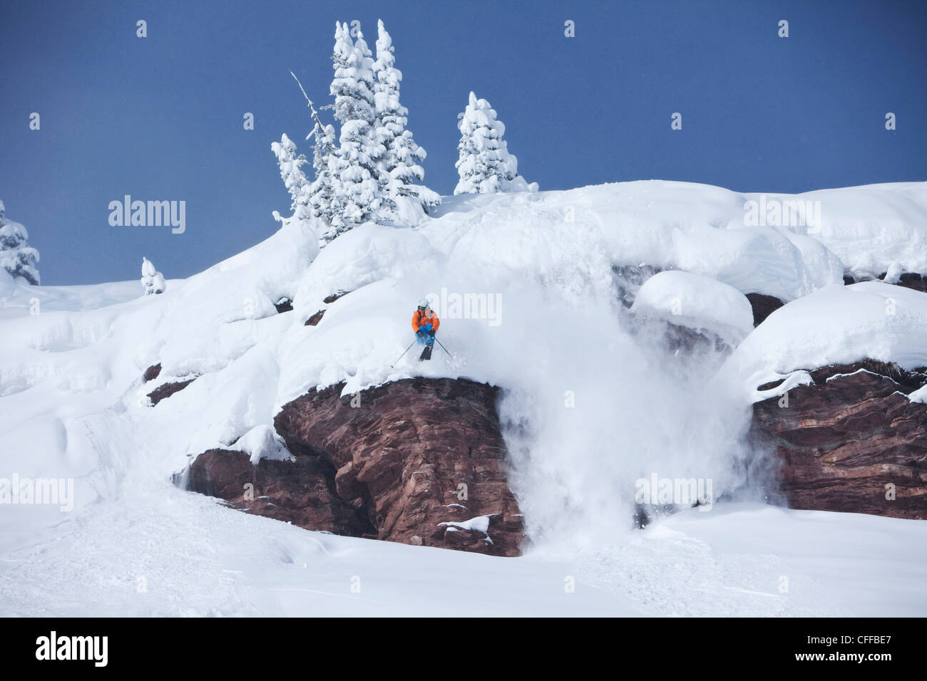 A athletic skier jumping off a cliff in the backcountry on a sunny powder day in Colorado. Stock Photo